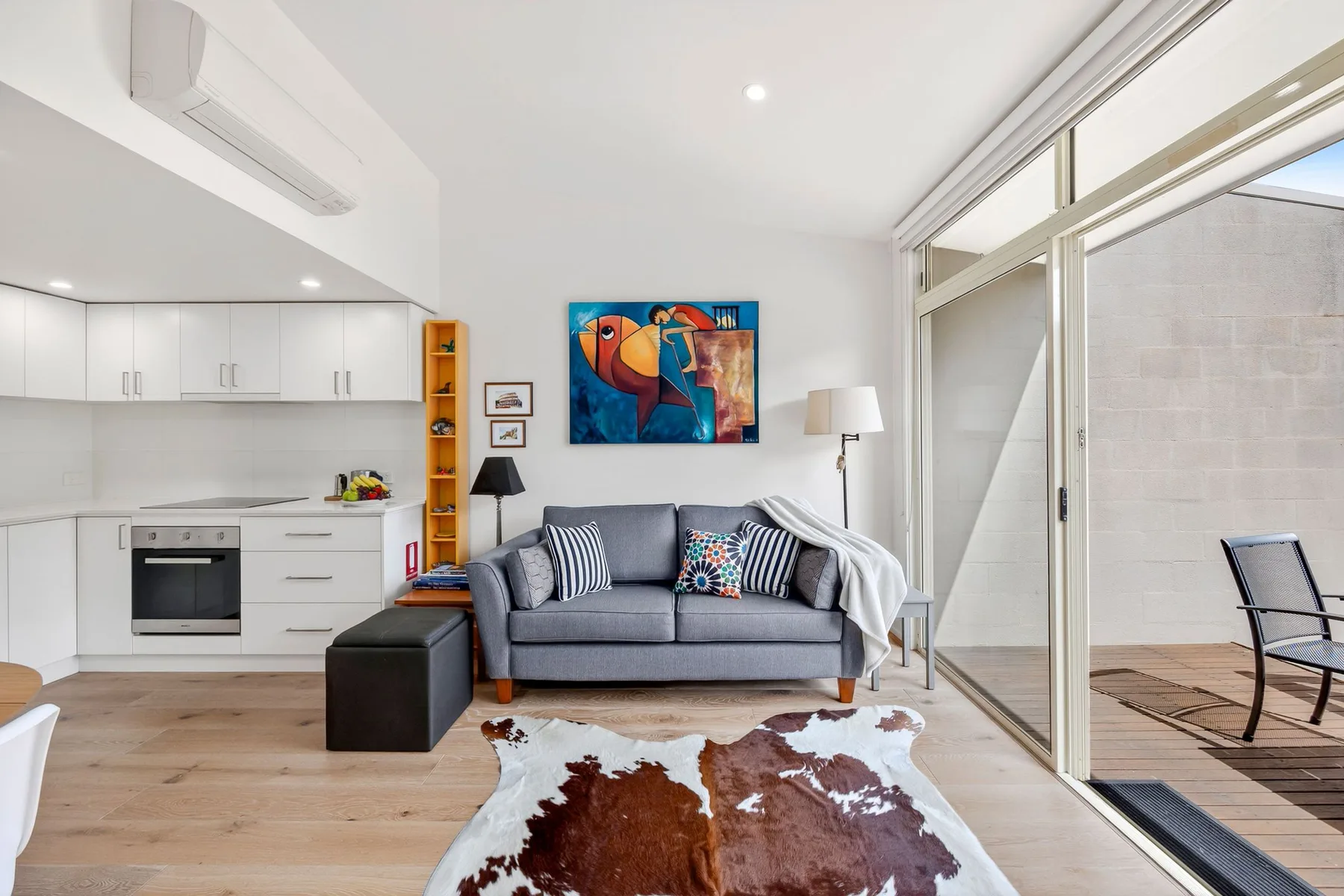 A bright living room with a gray sofa beside a modern kitchen.