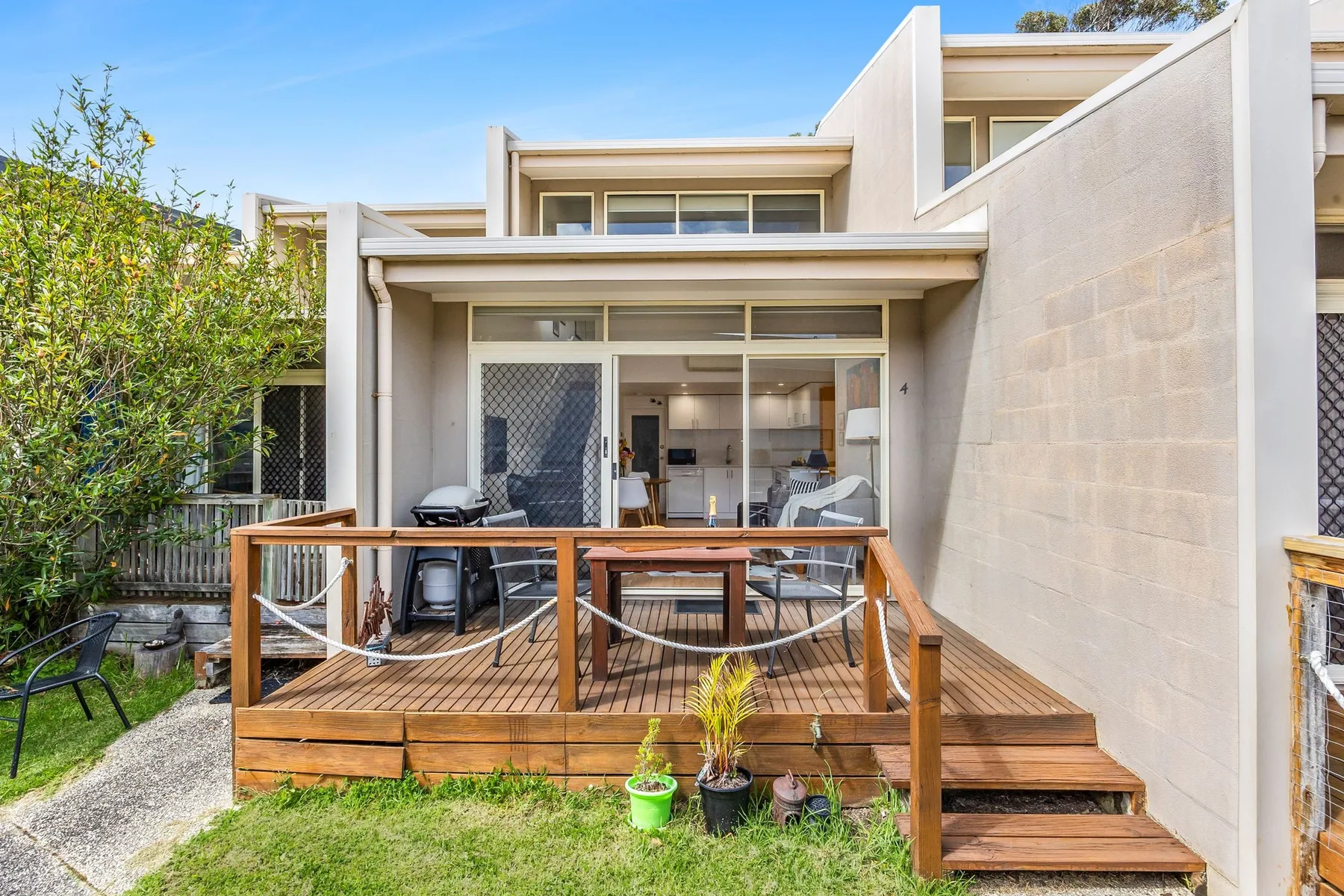 A modern house opens onto a wooden deck with outdoor seating.