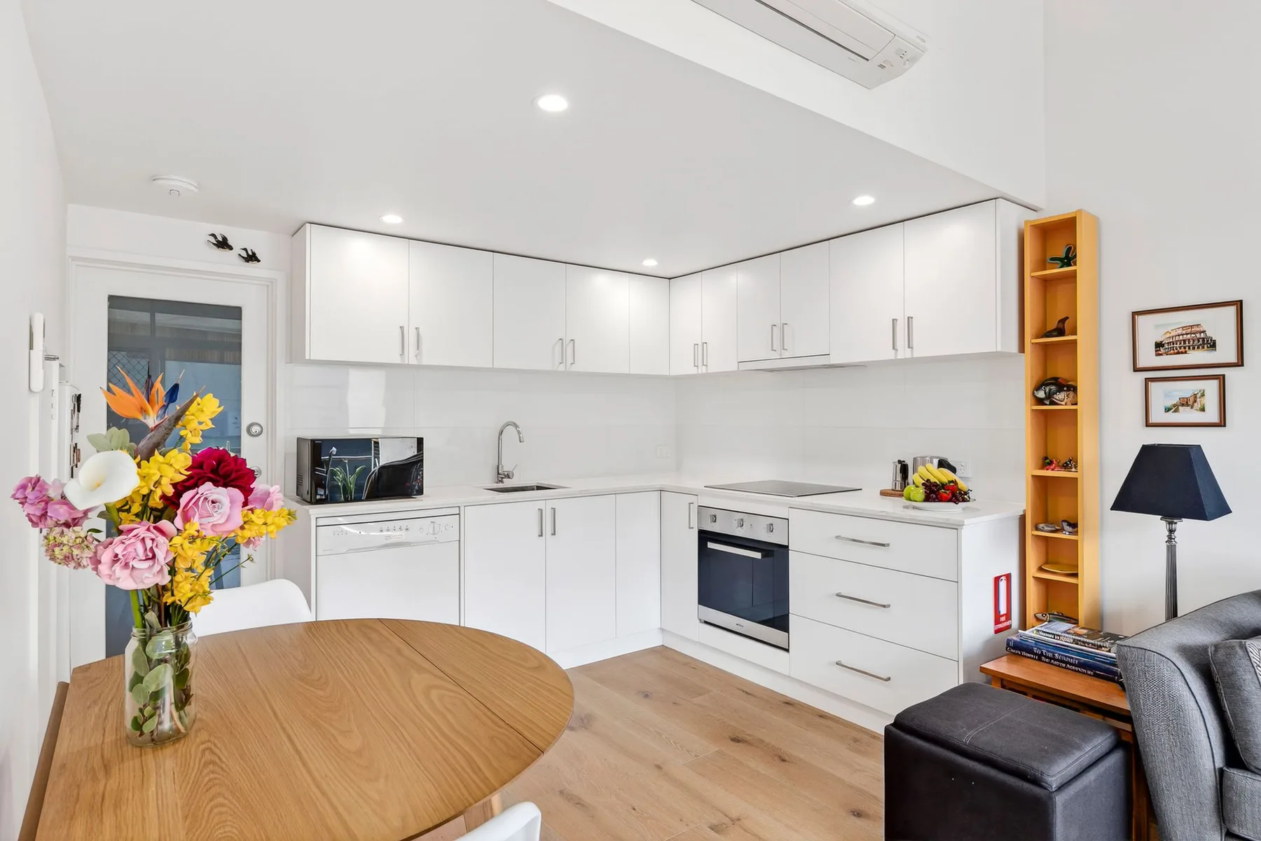 A bright kitchen with white cabinets, an oven, and a wooden dining table.