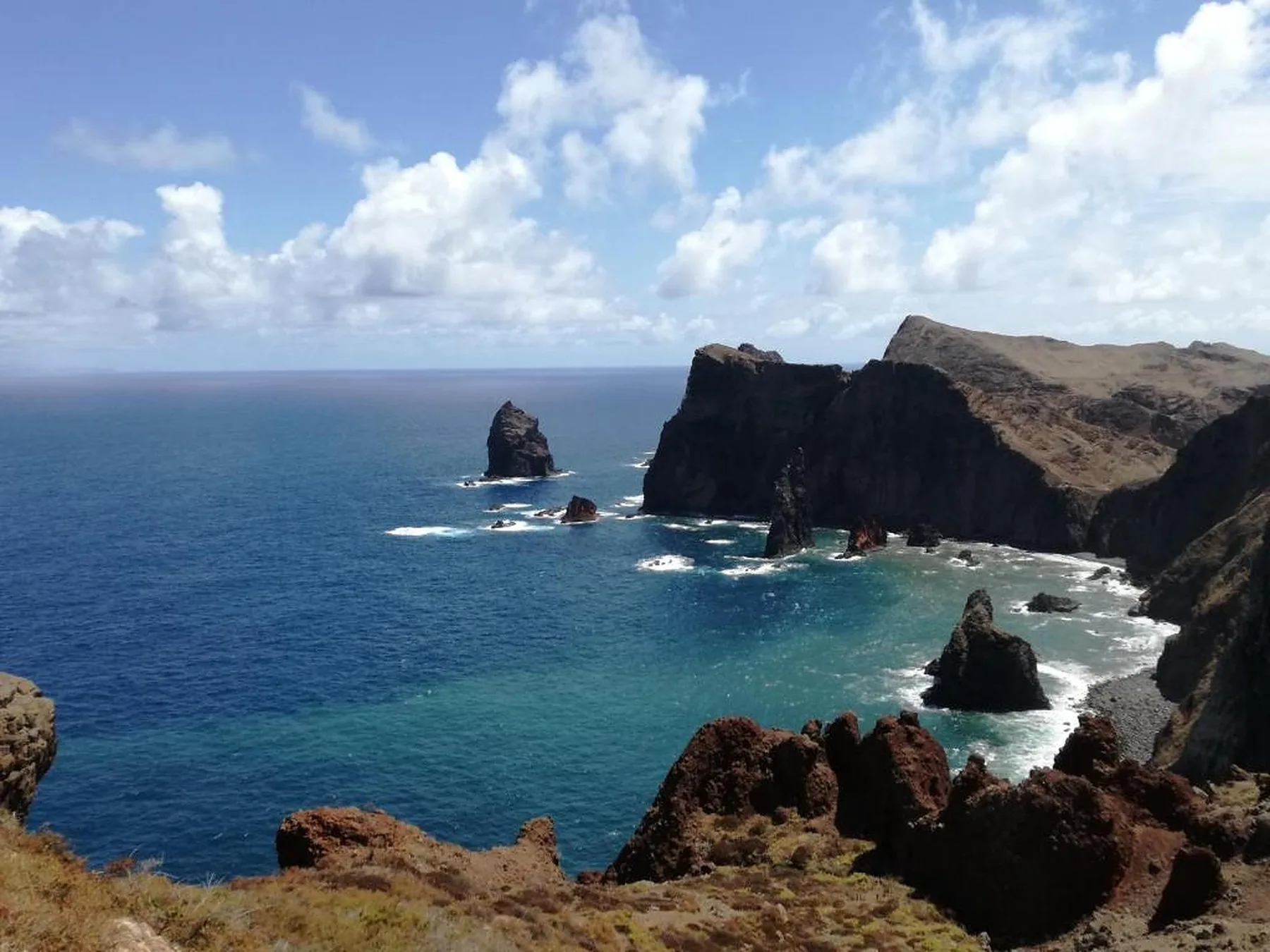 Una costa rocosa domina las aguas azules del océano bajo un cielo parcialmente nublado.