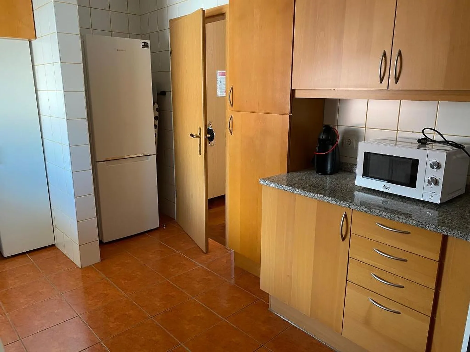 Una cocina con armarios de madera, un refrigerador y un microondas.