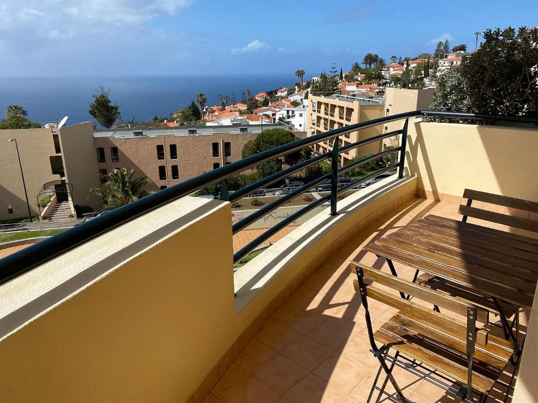 Un balcón soleado ofrece vistas de edificios en la ladera y del océano.