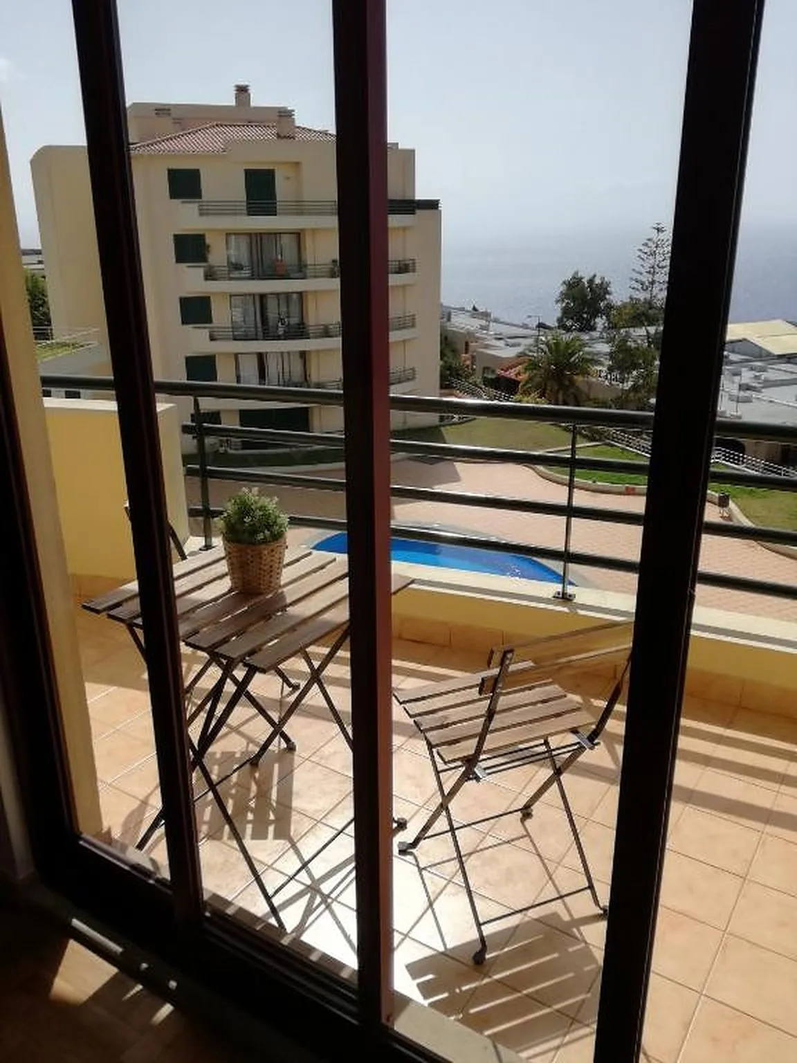 Un balcón embaldosado con asientos plegables da a una piscina y al mar.