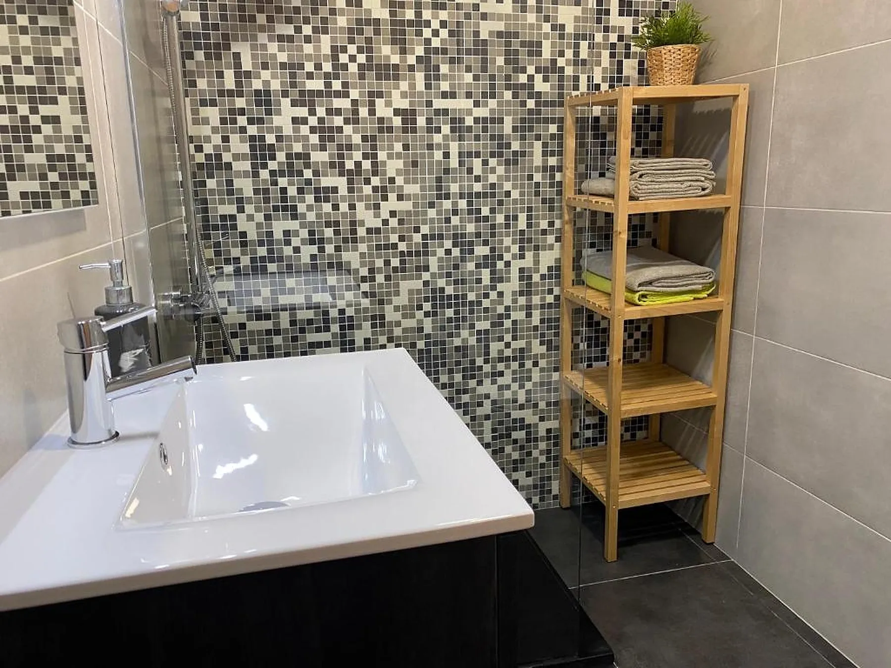 Un baño con lavabo blanco, pared de mosaico y estantería de madera.