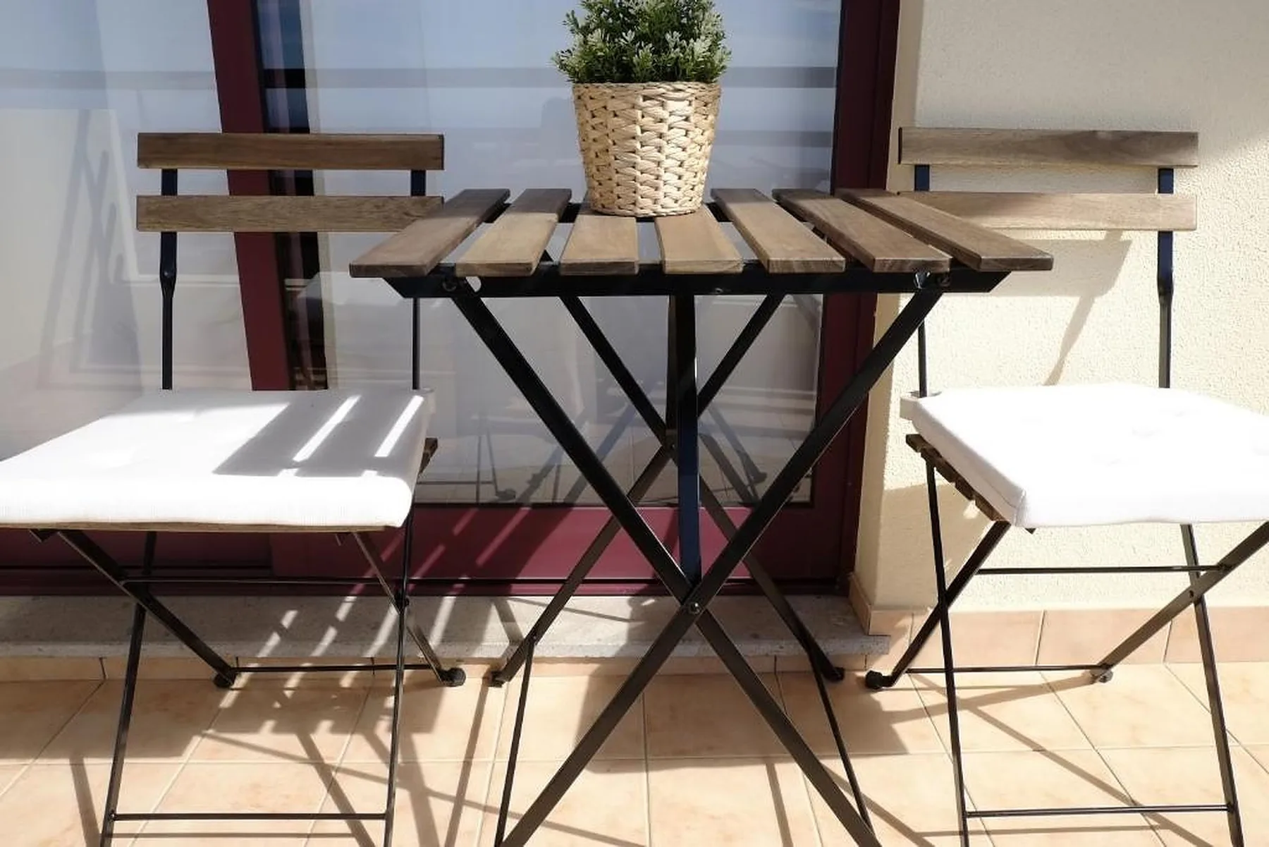 Una mesa pequeña y asientos al aire libre están frente a unas puertas de vidrio.