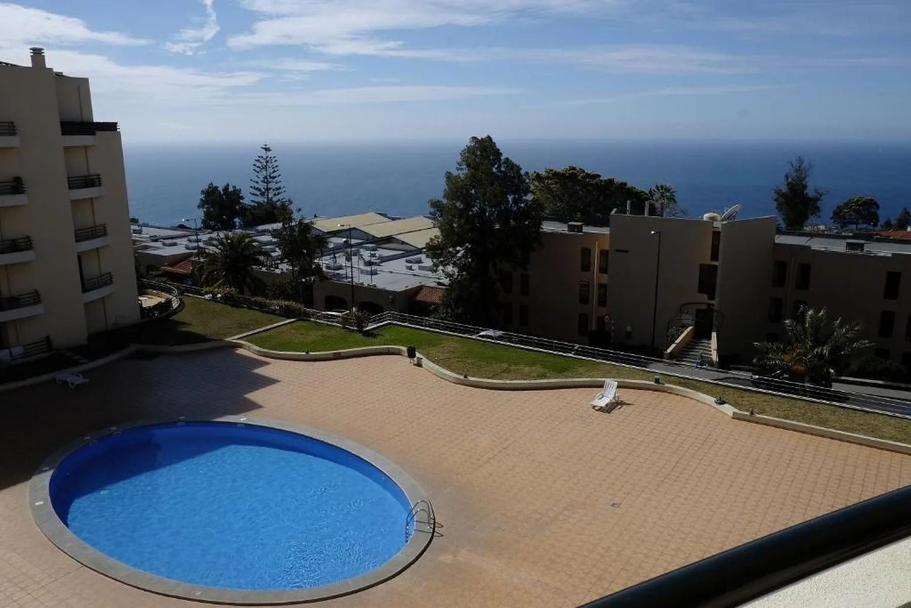 Una piscina al aire libre y una terraza pavimentada dan a edificios cercanos y al mar.