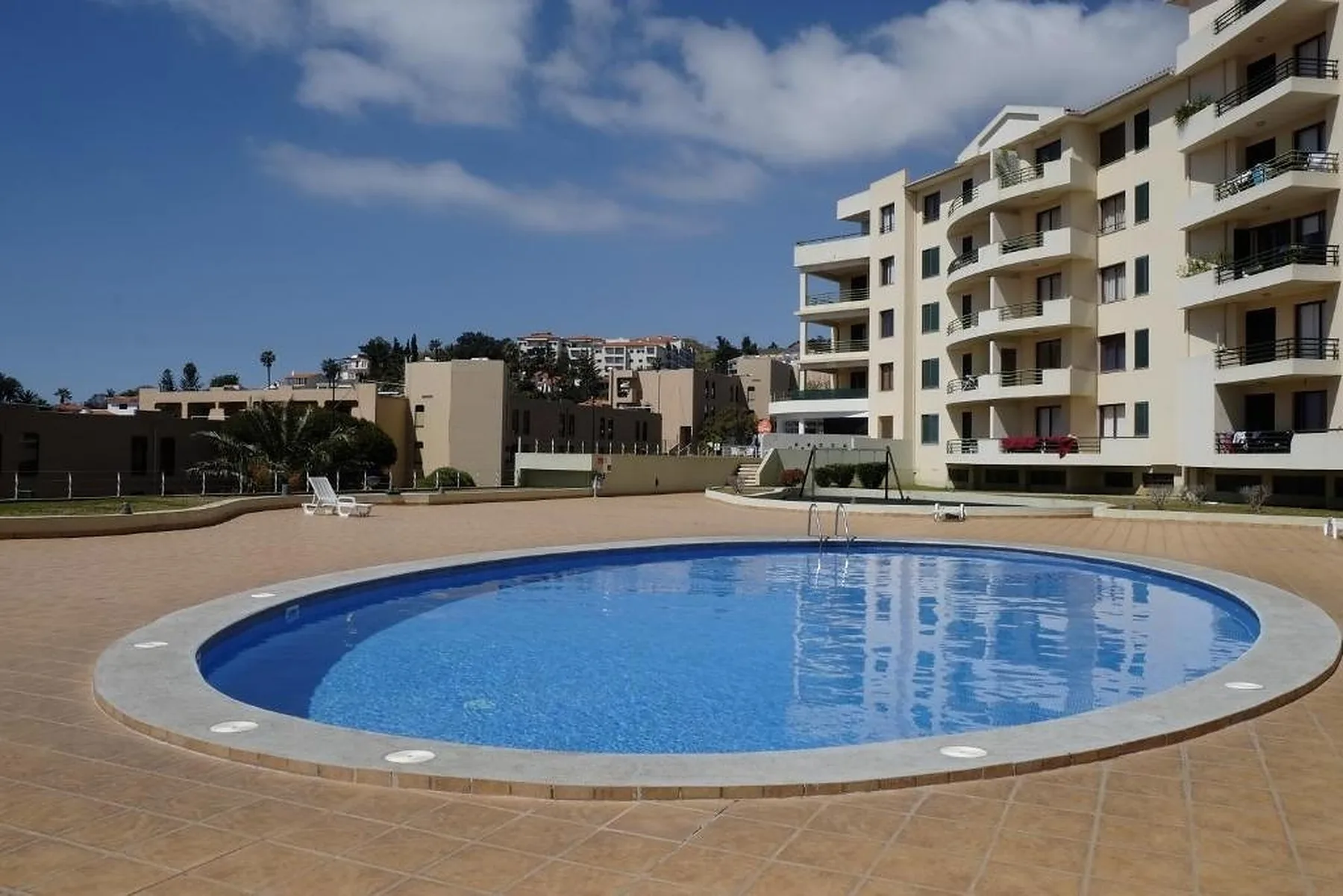 Piscina al aire libre junto a un edificio de apartamentos bajo un cielo parcialmente nublado.