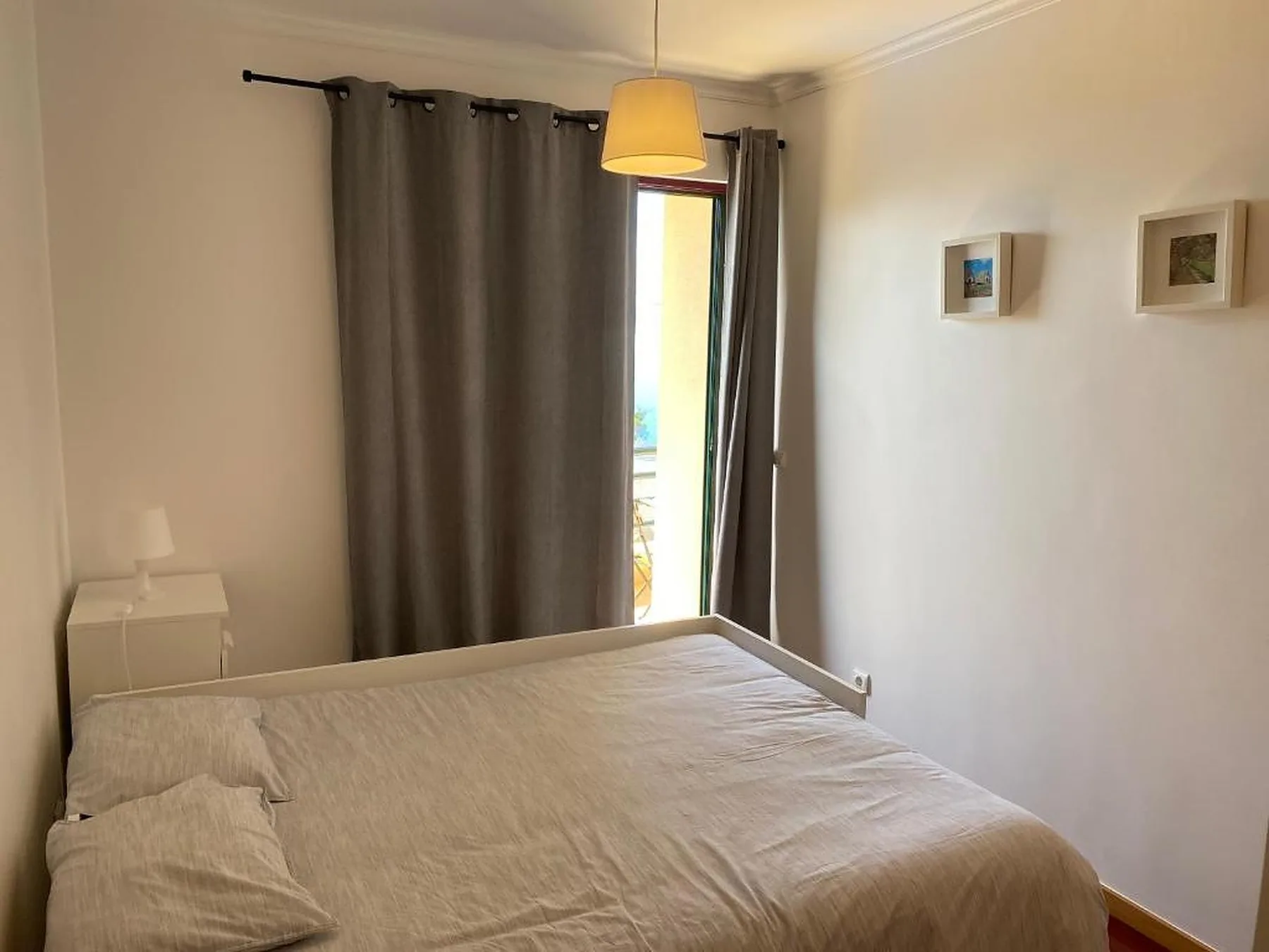 Un dormitorio con una cama, cortinas oscuras y cuadros en la pared.