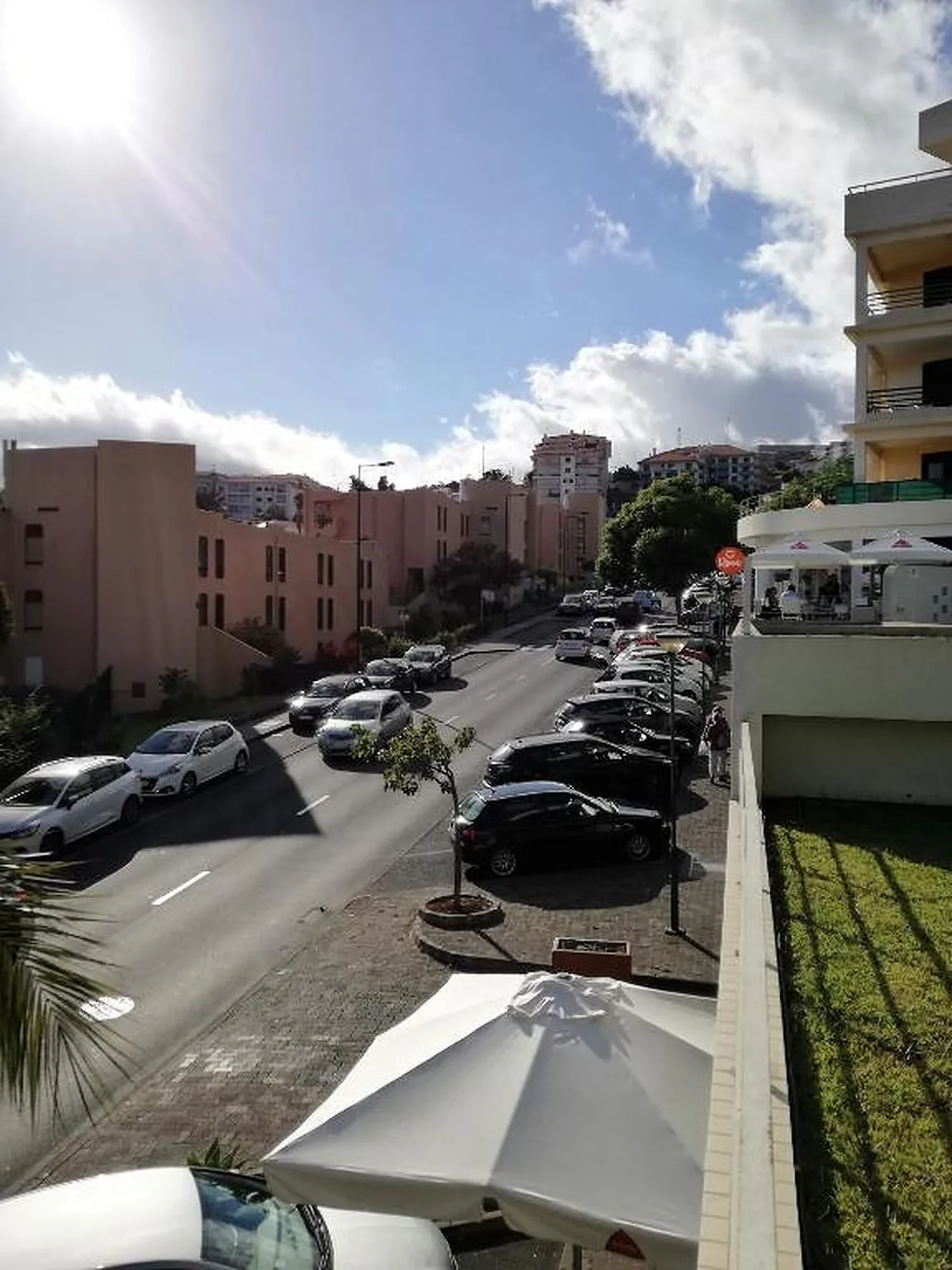 Una calle urbana soleada con coches aparcados y una sombrilla blanca.