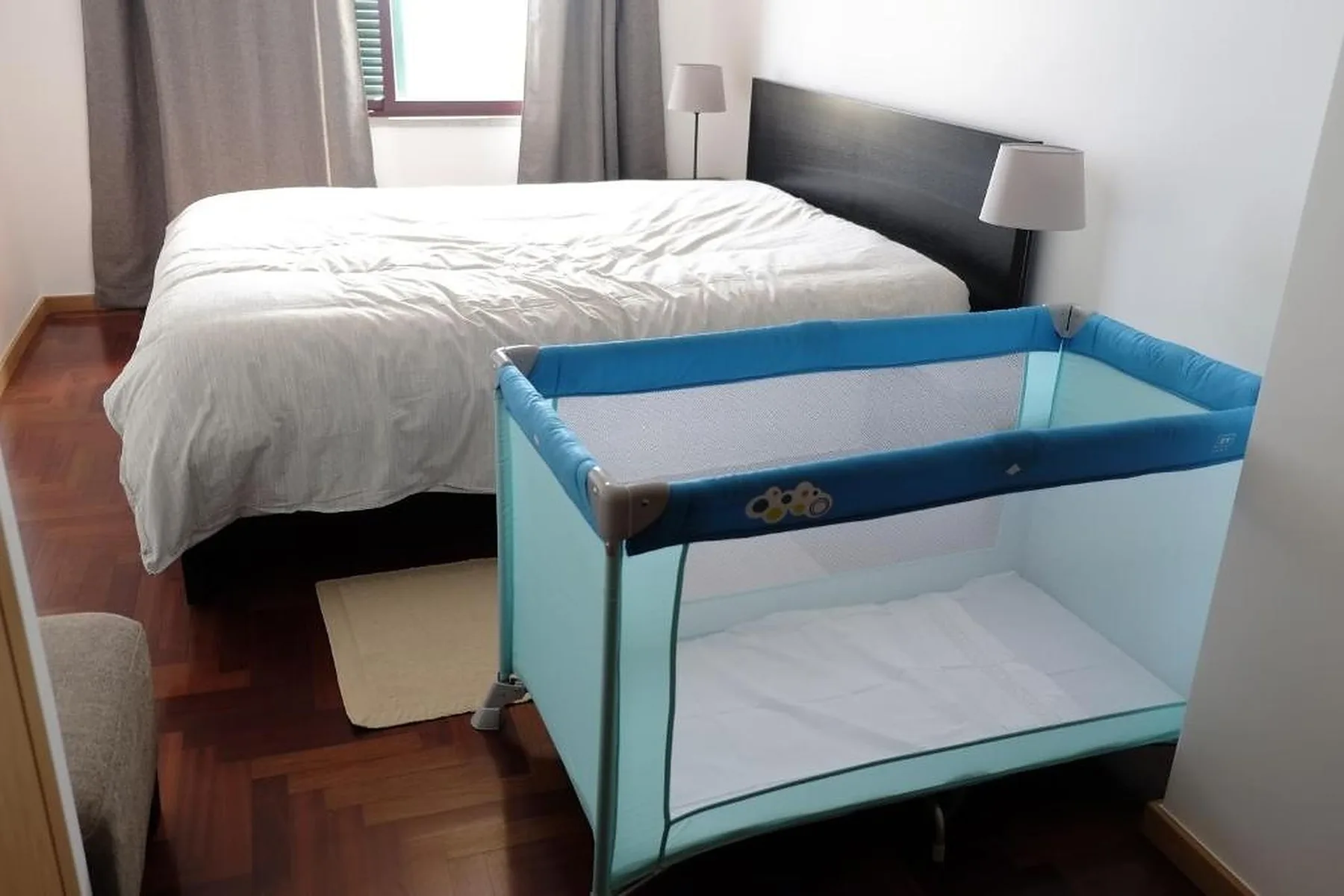 Un dormitorio con una cama y un corralito azul en primer plano.