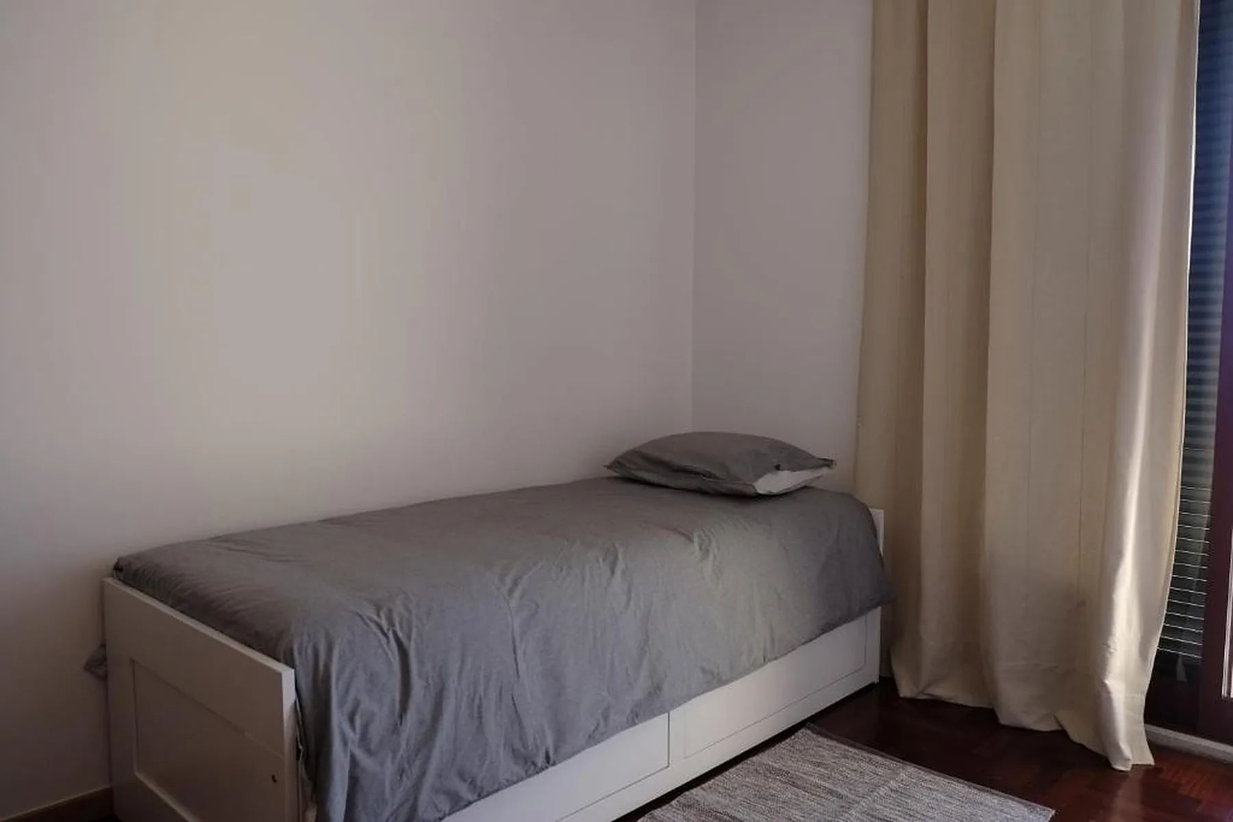 Un dormitorio con una cama individual junto a una ventana con cortinas.