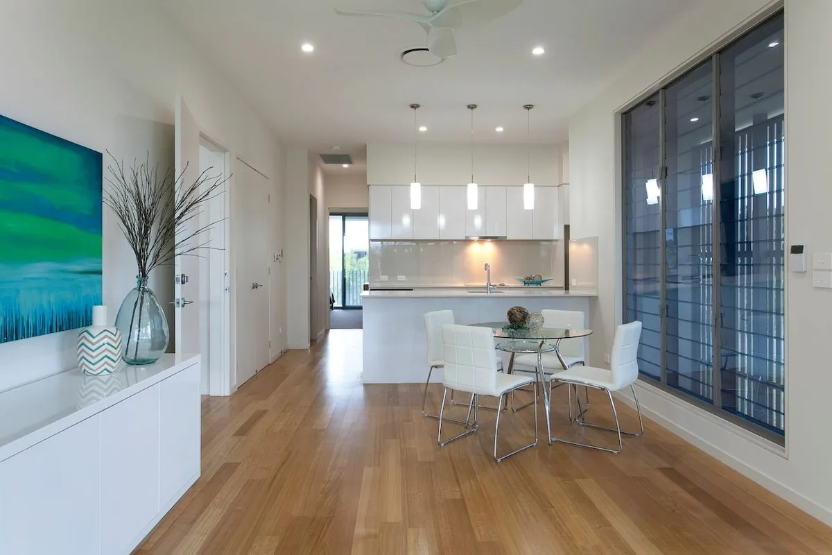 Cocina y comedor de concepto abierto con mesa de vidrio y asientos blancos.