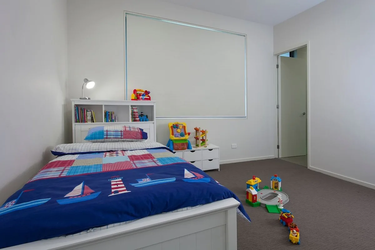 Un dormitorio con una colcha colorida, una estantería baja y juguetes en el suelo.