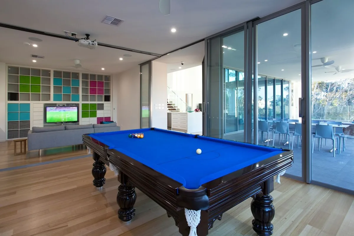 Una mesa de billar ocupa una luminosa sala de juegos junto a grandes ventanales.