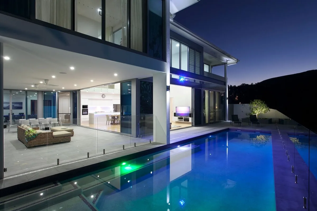 Casa moderna con piscina junto a una sala acristalada e iluminada.