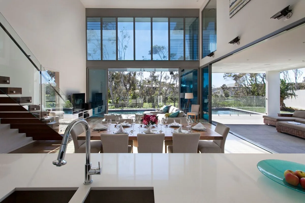 Una luminosa sala de estar y comedor de concepto abierto da a una piscina.