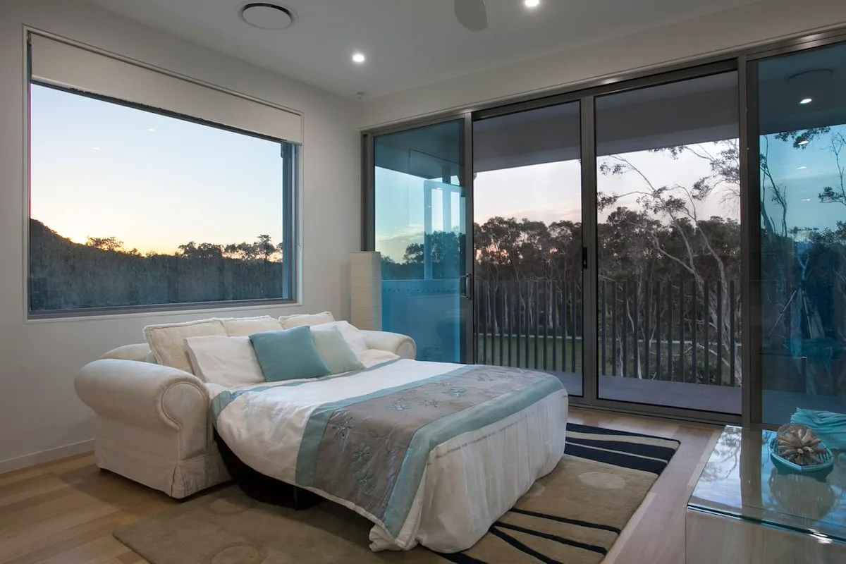 Un dormitorio con una cama junto a grandes ventanas que dan a los árboles.