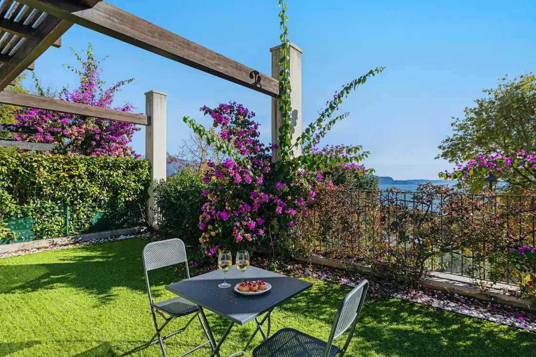 A garden patio with outdoor seating and flowering vines overlooking the water.
