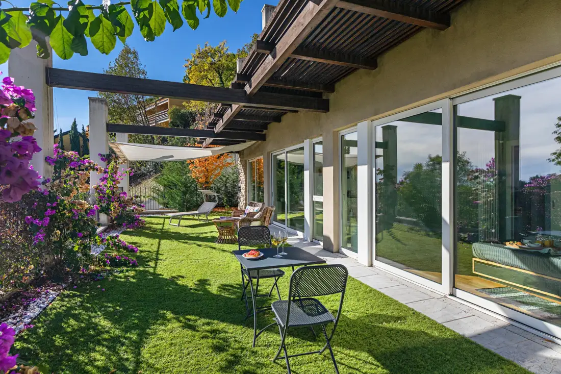 A garden patio with outdoor seating beside a house with glass doors.