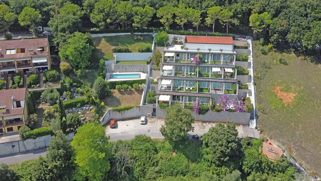 An aerial view shows a modern multi-level building with a swimming pool and surrounding greenery.
