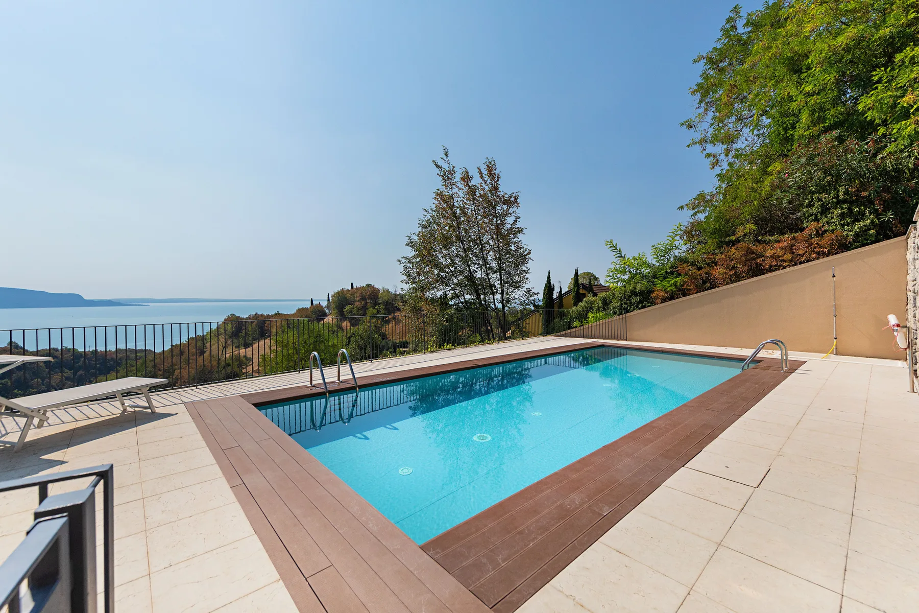 A swimming pool sits on a tiled outdoor terrace overlooking the water.