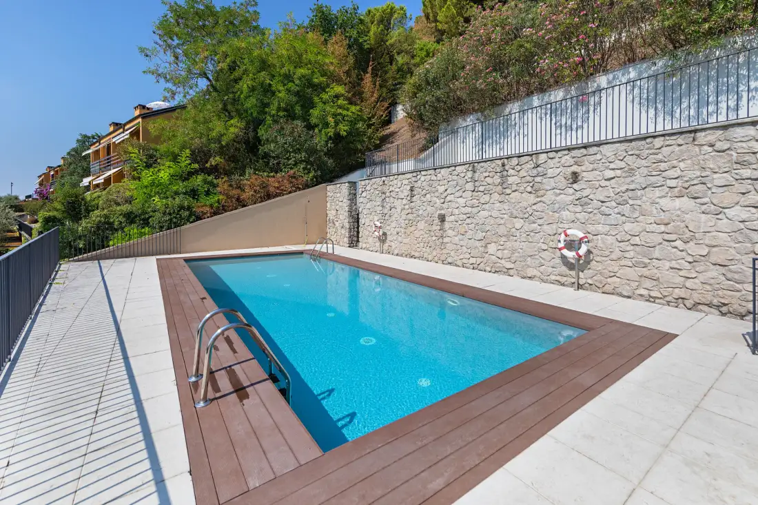 An outdoor swimming pool sits beside a stone wall and surrounding greenery.