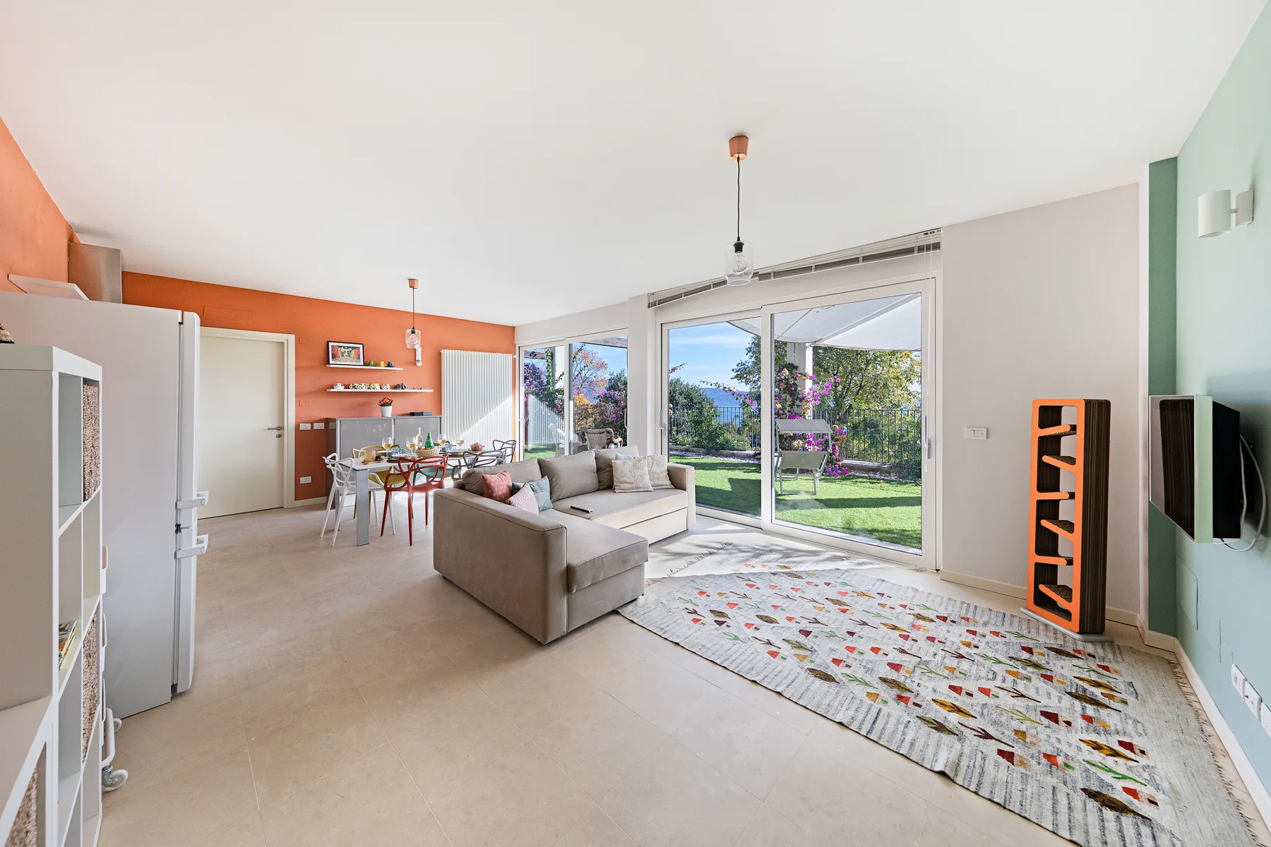 A bright living room opens onto a garden, with seating and a dining area.