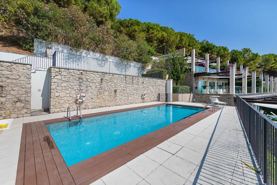 An outdoor swimming pool beside a stone wall and landscaped hillside.