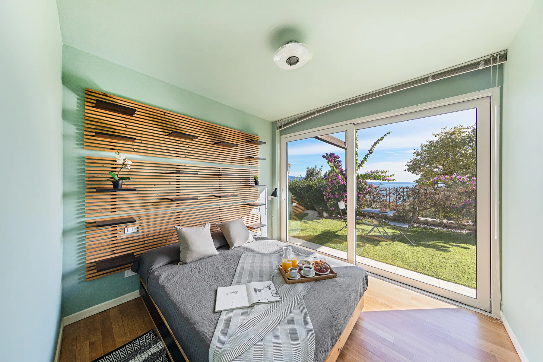 A bedroom with a bed beside large windows overlooking a garden.