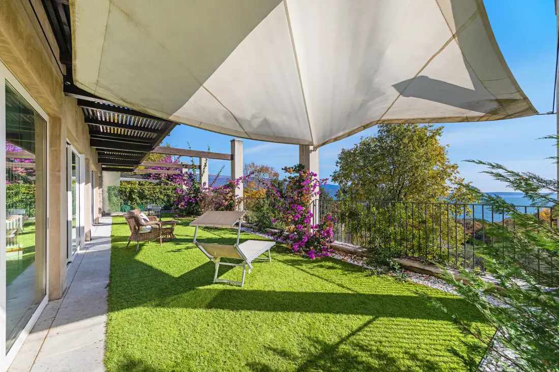 A garden patio with green lawn, outdoor seating, and a large shade canopy.