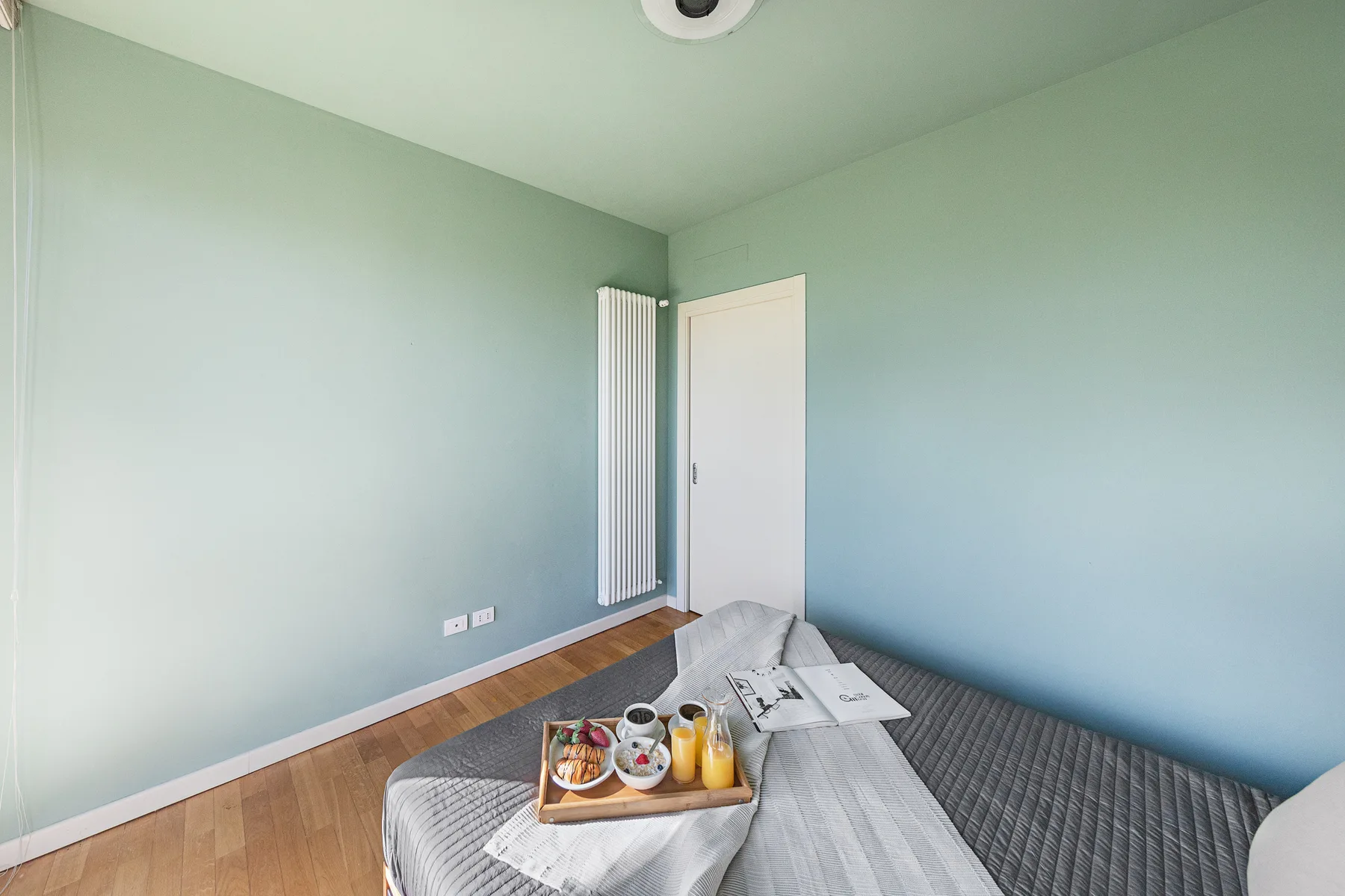 A bedroom with a low bed and a tray of drinks on the bed.