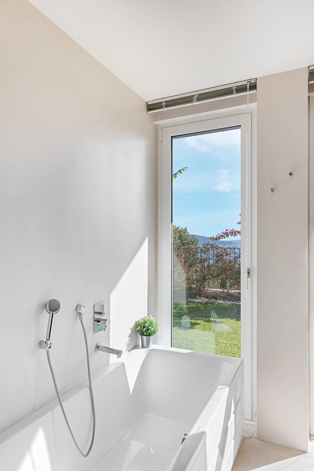 A bright bathroom features a bathtub beside a tall window overlooking greenery.