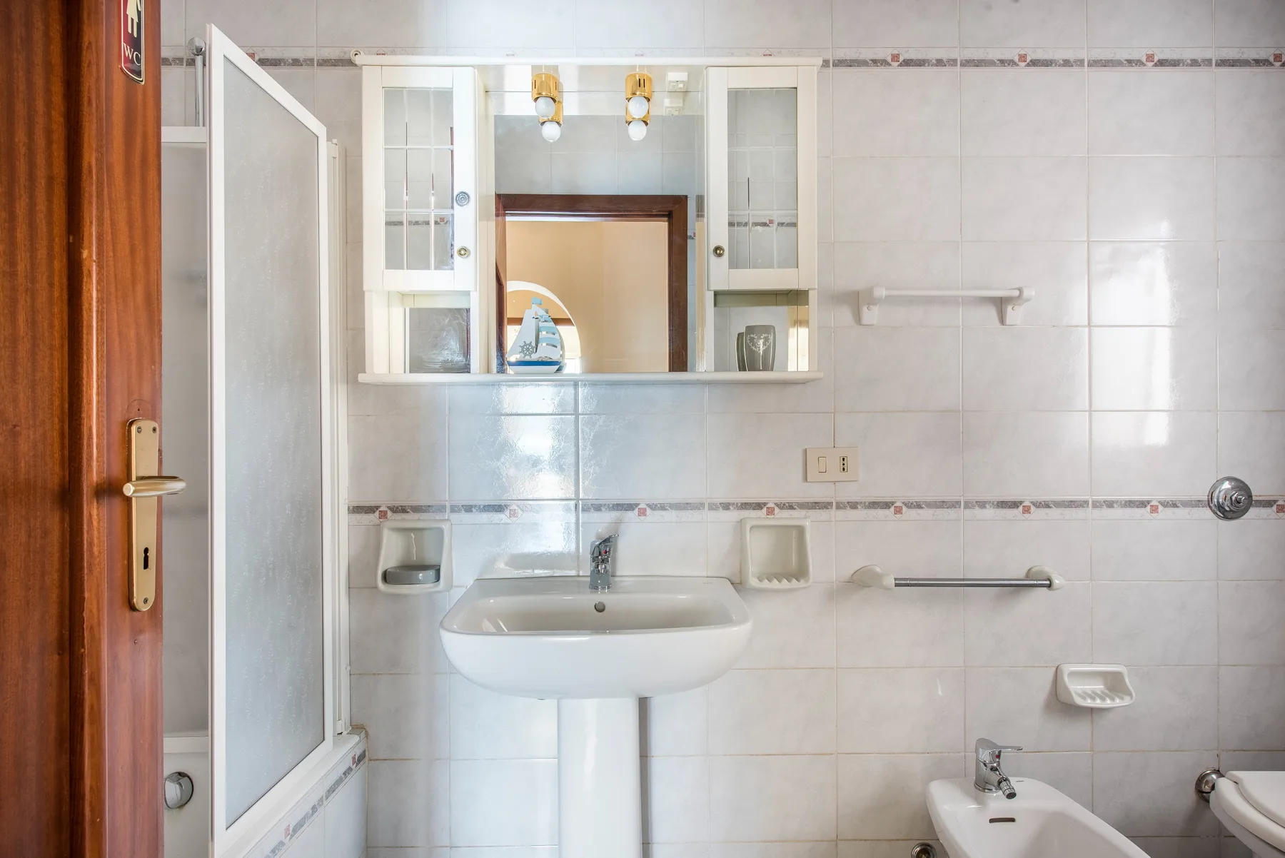 A tiled bathroom with a wall-mounted sink and a mirrored cabinet.