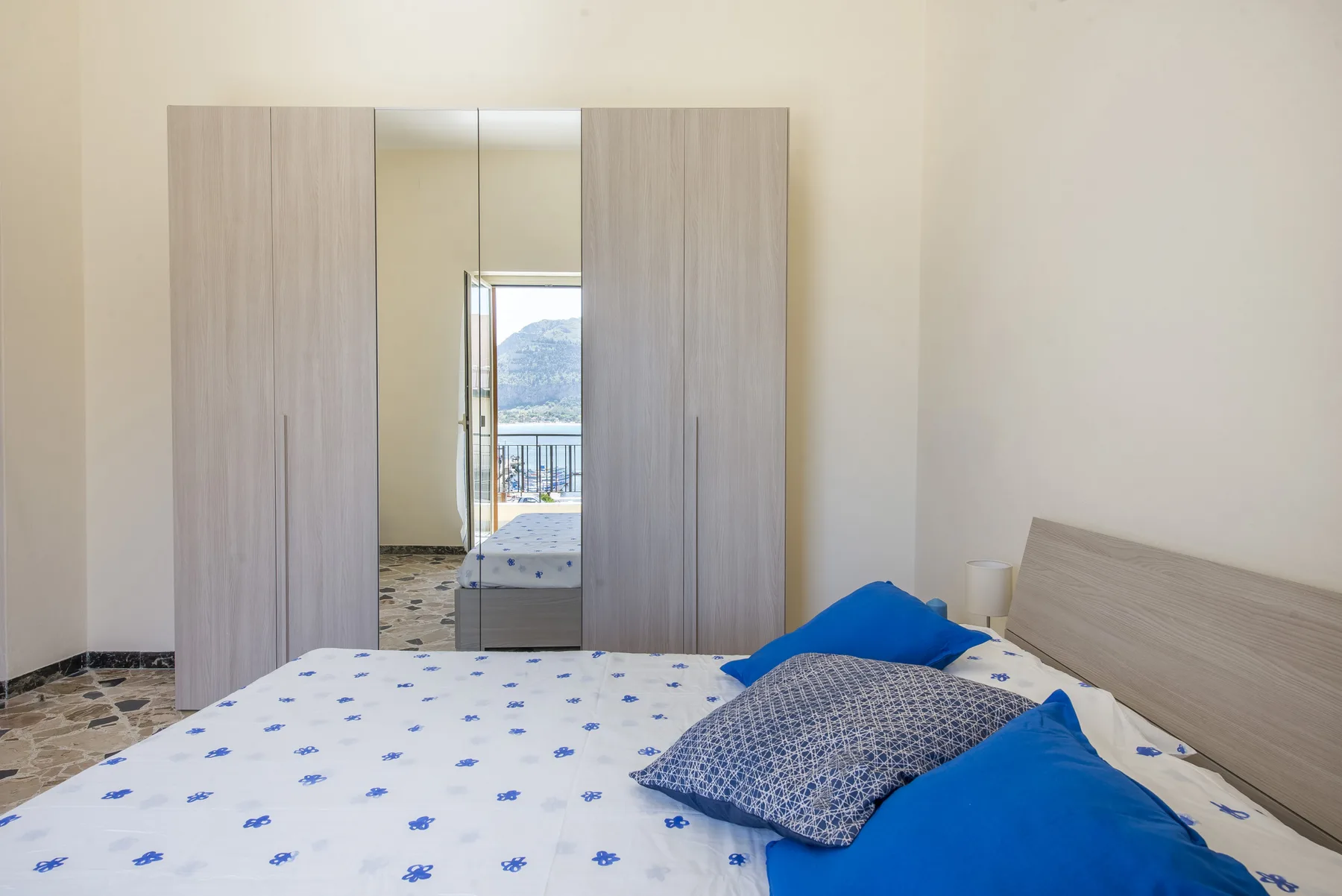 A bedroom with a patterned bedspread and a mirrored wardrobe.