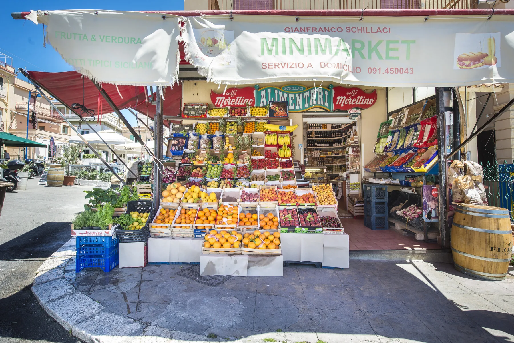 A small street market displays fresh produce and packaged goods beneath a storefront awning.