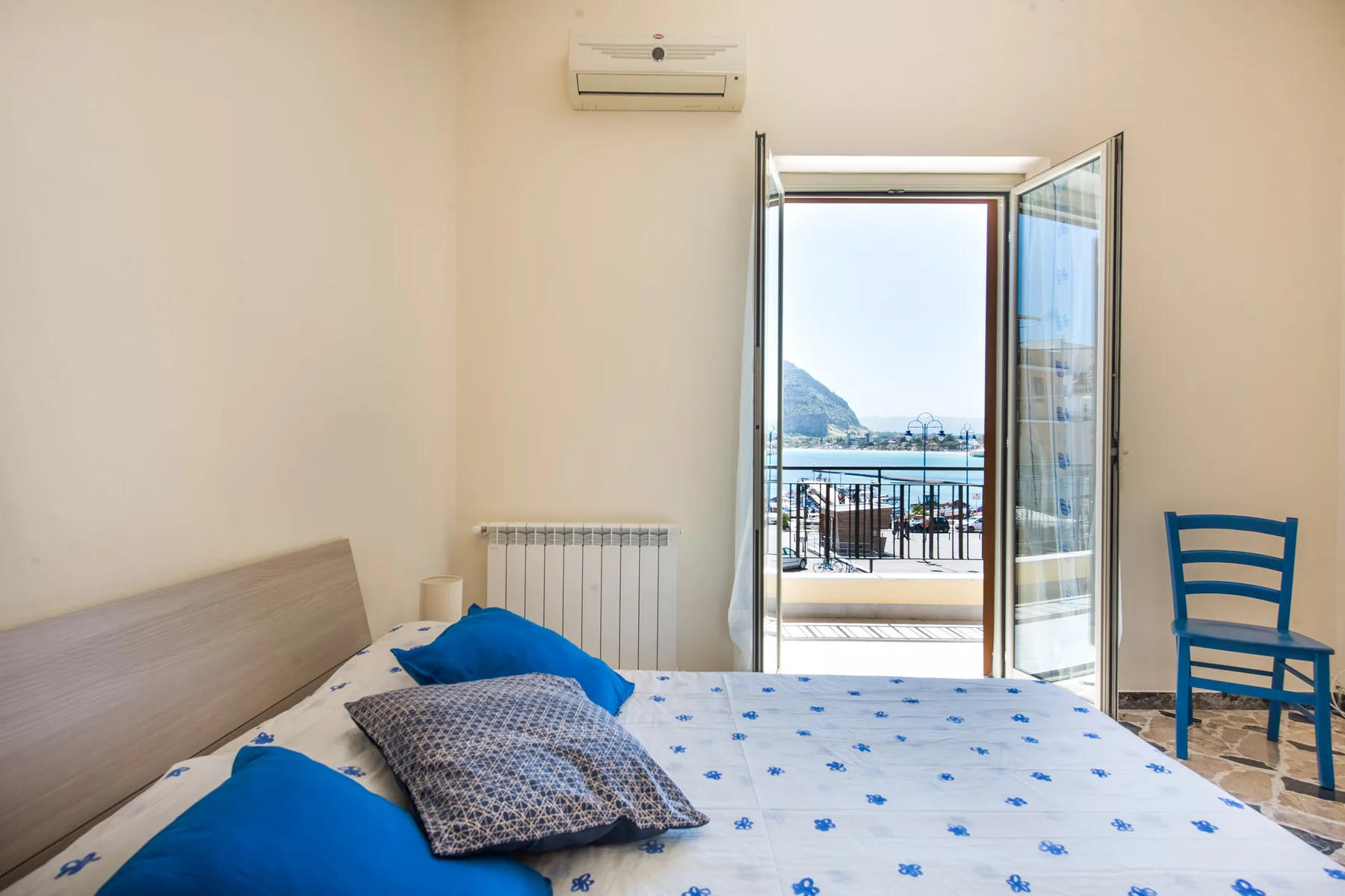 A bedroom opens through a glass door onto a balcony overlooking the water.