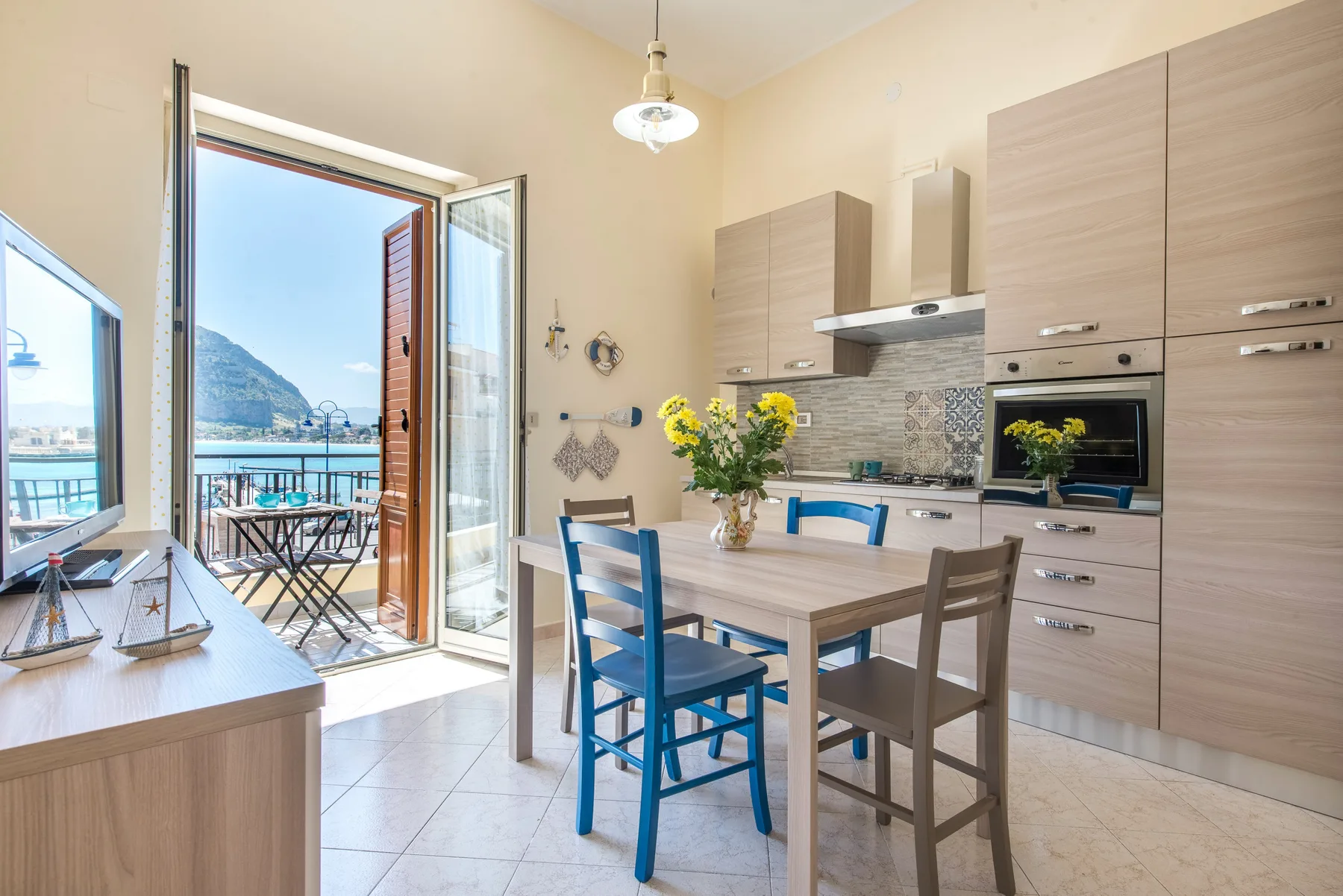 A bright kitchen and dining area opens onto a balcony with a mountain view.