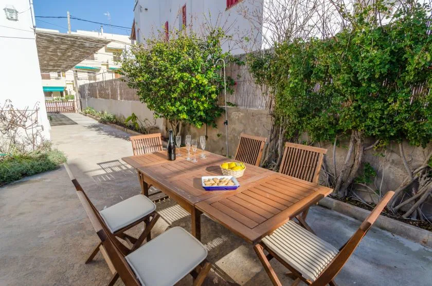 An outdoor patio features a wooden dining table surrounded by seating and greenery.
