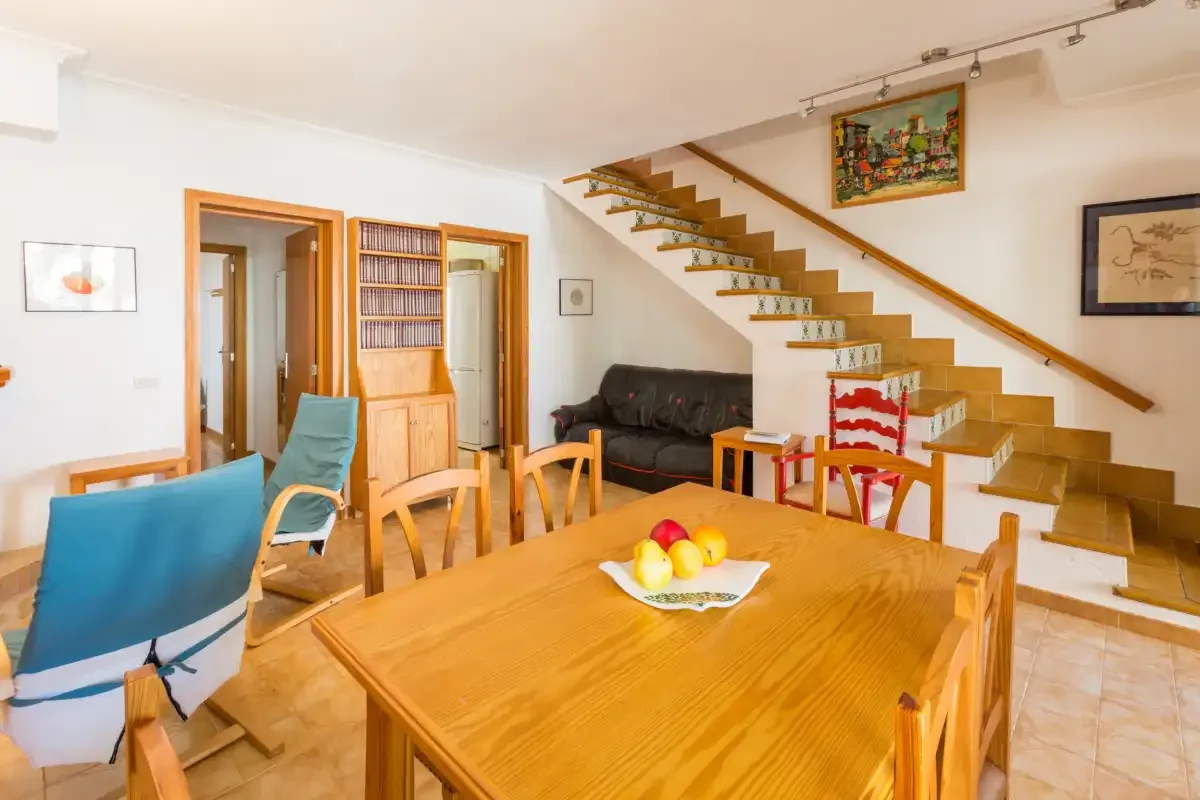 Comedor con mesa de madera y una escalera junto a la zona de estar.