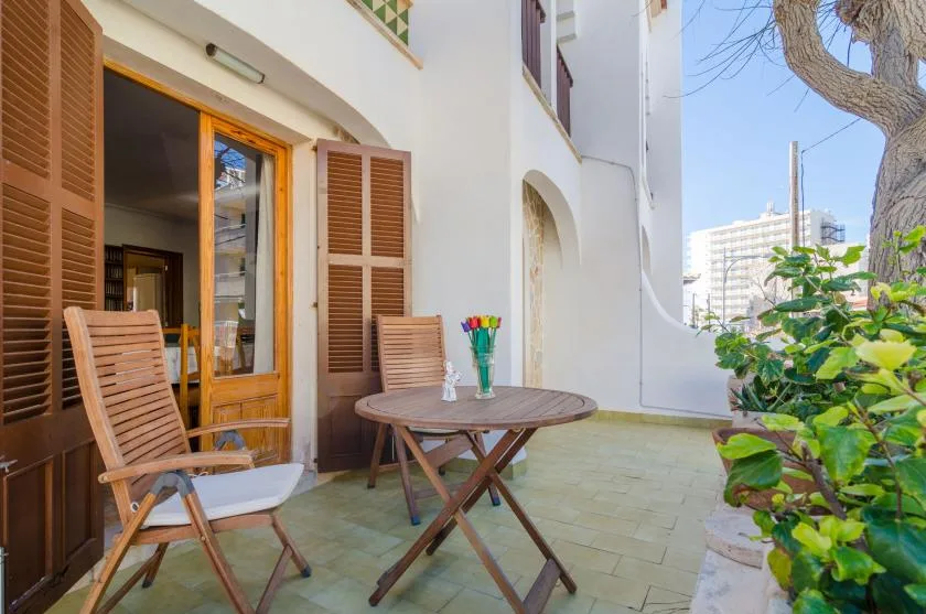 Un patio exterior embaldosado con asientos de madera y una puerta abierta.