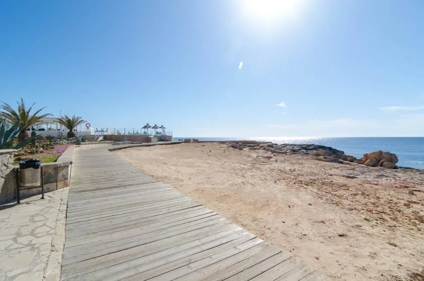 Una pasarela de madera bordea una playa abierta de arena junto al mar.