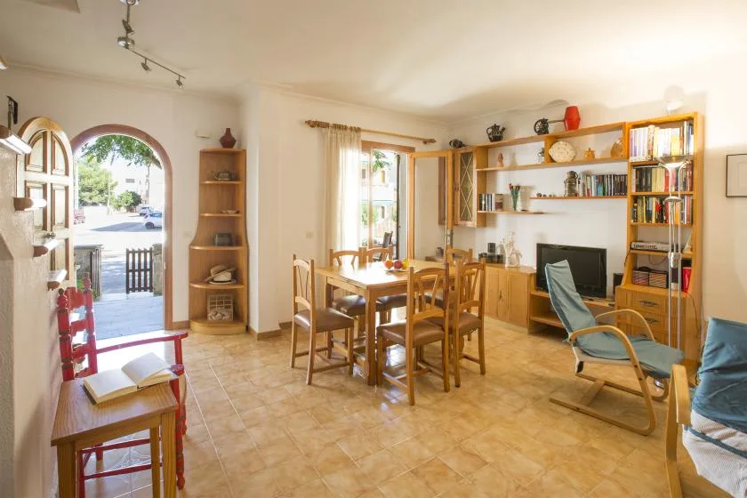 Comedor y sala de estar con una mesa de madera, estanterías y un televisor.