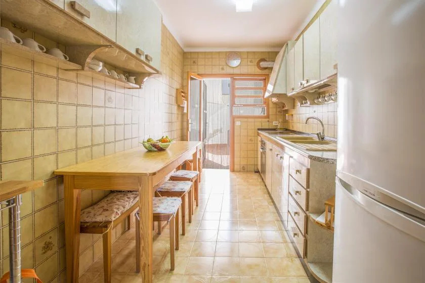Una cocina estrecha con azulejos, una mesa de madera, asientos y un fregadero.