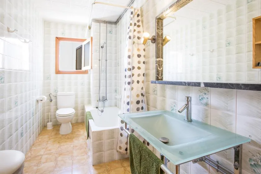 Un baño luminoso con azulejos, bañera, inodoro y lavabo de vidrio.