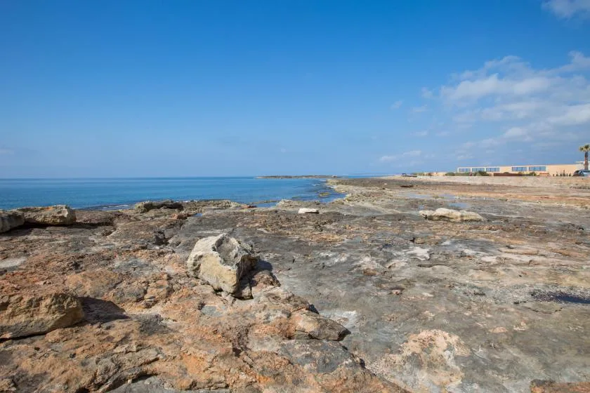 Una costa rocosa se extiende junto al mar azul bajo un cielo despejado.