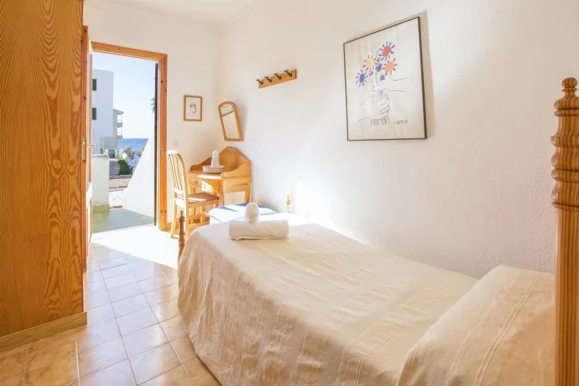 Un dormitorio luminoso con una cama y un pequeño escritorio de madera junto a la puerta abierta.