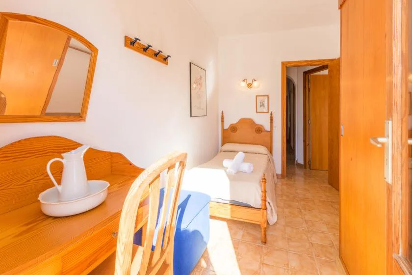 Un dormitorio con una cama individual, muebles de madera y una puerta al pasillo.