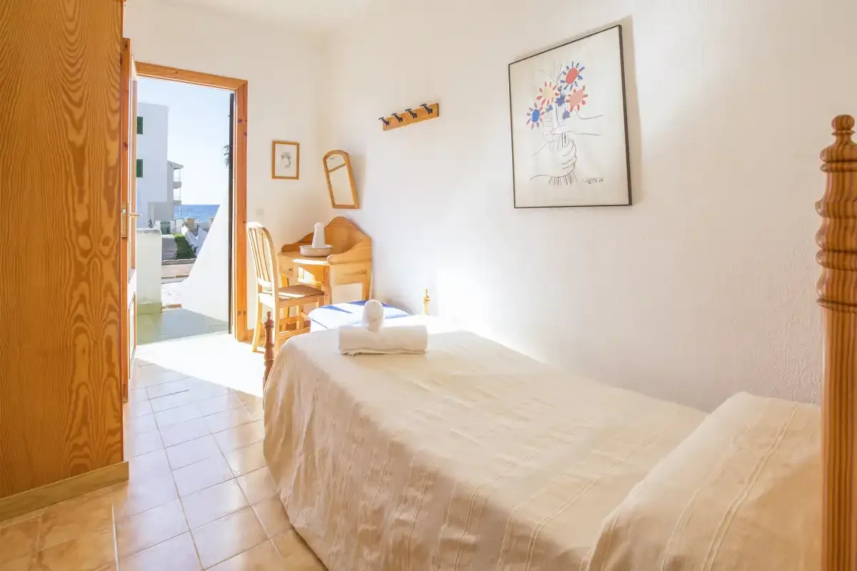 Un dormitorio luminoso con una cama bien hecha y un pequeño escritorio junto a la puerta abierta.