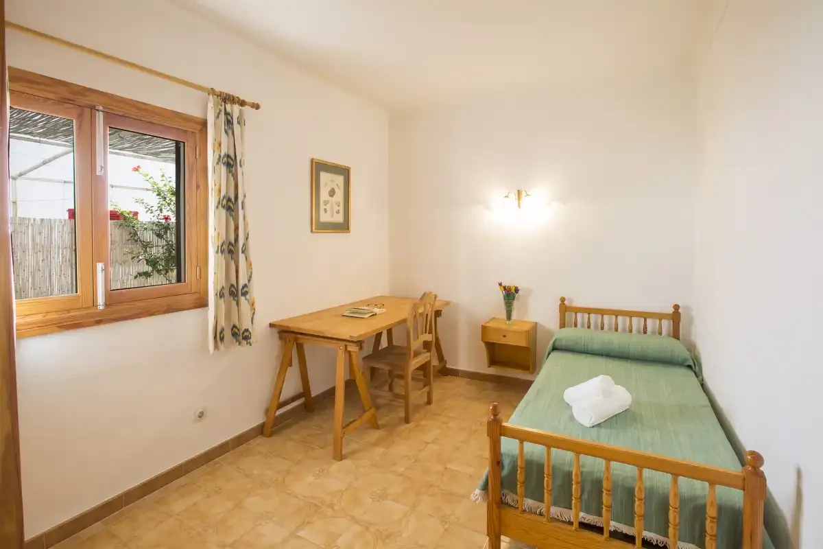 Un dormitorio con una cama individual y un escritorio de madera junto a la ventana.