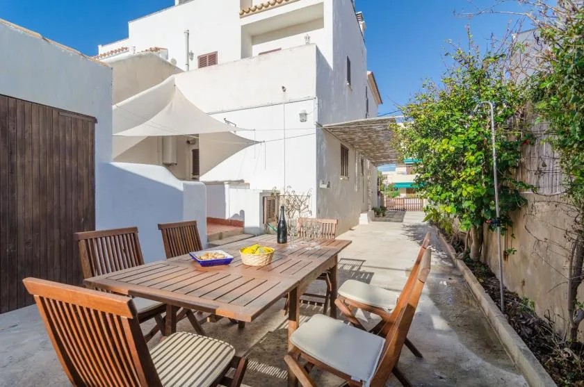 An outdoor dining area with a wooden table and seating beside a white building.